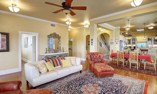 Cozy living area in a Gulf Waters beach house, featuring a comfortable white sofa with colorful pillows, a red armchair, a decorative rug, and an open layout leading to a dining area, showcasing modern comforts for vacationers.