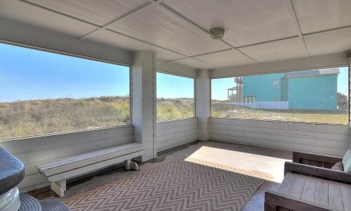 Screened porch of a beach house at Gulf Waters Beach Front RV Resort, featuring a view of sandy dunes and Mustang Island, designed for relaxation during a beach getaway.
