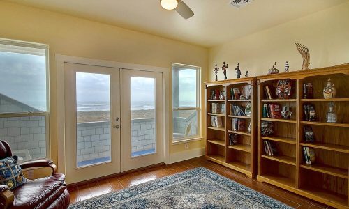 Cozy interior of a beach house at Gulf Waters Beach Front RV Resort, featuring a bookshelf, comfortable seating, and large windows with ocean views.