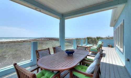Beach house patio with wooden dining table and chairs, overlooking Mustang Island's sandy shores and ocean view, ideal for coastal getaways at Gulf Waters Beach Front RV Resort.
