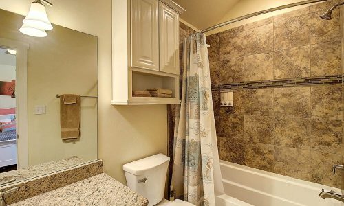 Modern bathroom with granite countertop, bathtub, shower curtain, and decorative tiles, featuring stylish lighting and organized storage, reflecting the comfort of Gulf Waters Beach Front RV Resort accommodations.