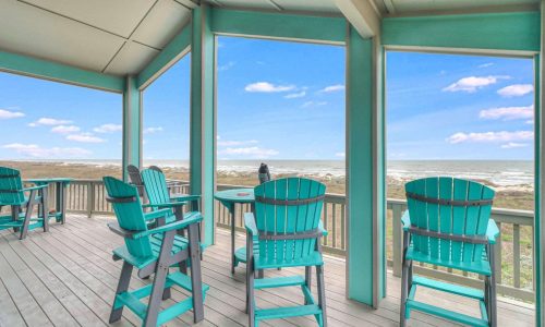 Beach house deck with turquoise chairs overlooking sandy shores and ocean at Gulf Waters Beach Front RV Resort.