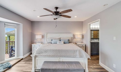 Cozy beach house bedroom with a king-size bed, modern furnishings, bedside lamps, and access to a private balcony, reflecting the comfort and style of Gulf Waters Beach Front RV Resort accommodations.