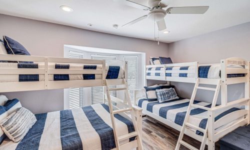 Bunk room in beach house with white wooden bunk beds and blue-striped bedding, designed for family or group stays at Gulf Waters Beach Front RV Resort.