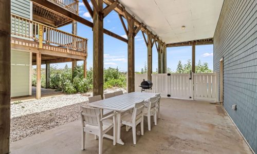 Outdoor patio area of a beach house at Gulf Waters Beach Front RV Resort, featuring a white dining table and chairs, grill, and surrounding greenery, ideal for family gatherings and vacations.