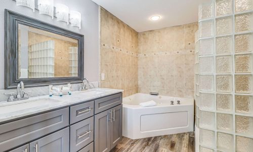 Contemporary bathroom featuring a bathtub, double sink vanity, and glass block wall for privacy.