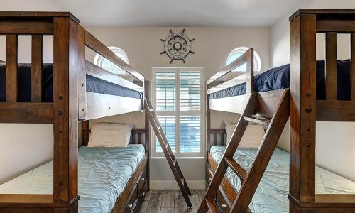 Bunk beds in a beach house rental at Gulf Waters Beach Front RV Resort, featuring wooden frames, light blue bedding, and nautical decor, ideal for family vacations and group trips.