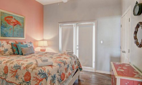 Cozy beach house bedroom with tropical decor, featuring a colorful quilt, bedside lamp, and large windows leading to a private outdoor space, ideal for a relaxing stay at Gulf Waters Beach Front RV Resort.
