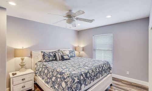 Cozy bedroom in Gulf Waters Beach Front RV Resort beach house featuring a king-sized bed with nautical-themed bedding, bedside lamps, and natural light from a window, ideal for a relaxing vacation getaway.