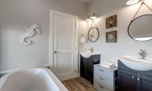 Modern bathroom interior featuring dual sinks, decorative mirrors, and nautical-themed decor, emphasizing comfort and style for Gulf Waters Beach Front RV Resort rentals.