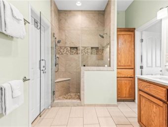 Bright bathroom with walk-in shower, wooden cabinets, and tiled floor.