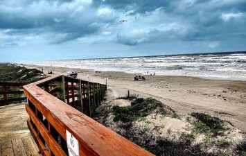 Scenic view from the private boardwalk at Gulf Waters Beach Front RV Resort, showcasing the sandy beach, rolling waves, and overcast sky, emphasizing the resort's coastal charm and access to the Gulf.