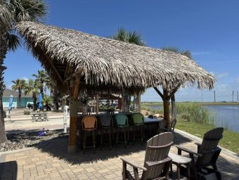 Beachfront tiki hut at Gulf Waters RV Resort with seating and water view.
