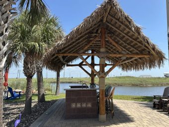 Beachfront tiki hut at Gulf Waters RV Resort with palm trees and water view.