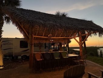 Beachfront RV resort with thatched roof pavilion and outdoor seating at sunset.
