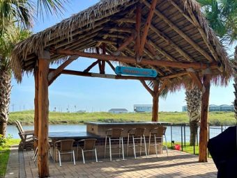 Beachfront tiki hut with seating and water view at Gulf Waters RV Resort.