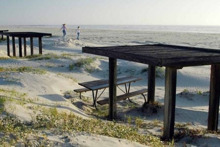 Beachfront view with wooden picnic tables and ocean in the background.