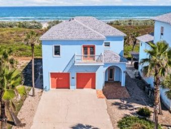 Beachfront RV resort lot with two-story blue house and palm trees.