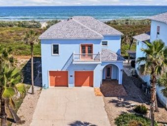 Beachfront RV resort lot with two-story blue house and palm trees.