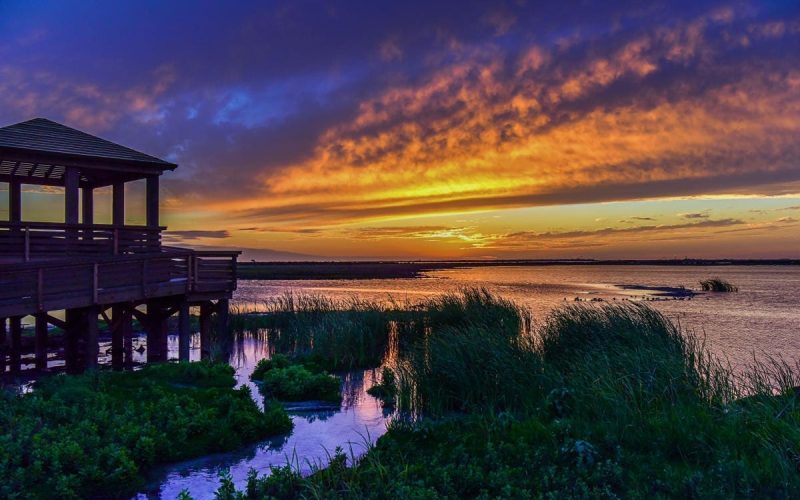 Scenic sunset over water at Leonabelle Turnbull Birding Center, showcasing vibrant colors and lush vegetation, highlighting the natural beauty near Gulf Waters Beach Front RV Resort in Port Aransas.