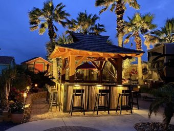 Tropical outdoor bar area at Gulf Waters Beach Front RV Resort, featuring palm trees, ambient lighting, and seating, highlighting resort amenities for potential RV lot owners.