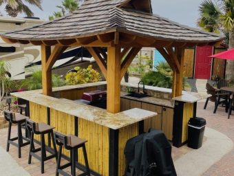 Outdoor tiki bar with seating, surrounded by tropical landscaping, at Gulf Waters Beach Front RV Resort, enhancing the vacation experience.