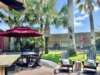 Patio area with outdoor seating, umbrella, and palm trees at Gulf Waters Beach Front RV Resort, showcasing a relaxing vacation atmosphere.