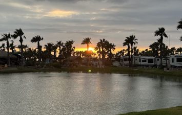 Scenic sunset over water with palm trees at Gulf Waters Beach Front RV Resort.