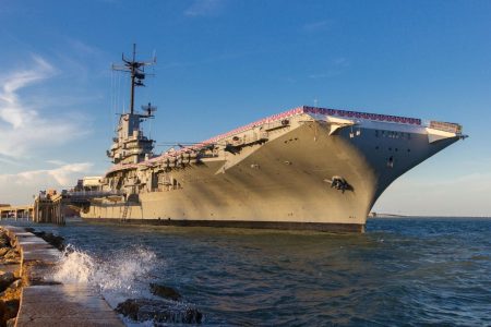 USS Lexington aircraft carrier museum docked in Corpus Christi, Texas, with waves splashing against the pier and a clear blue sky.